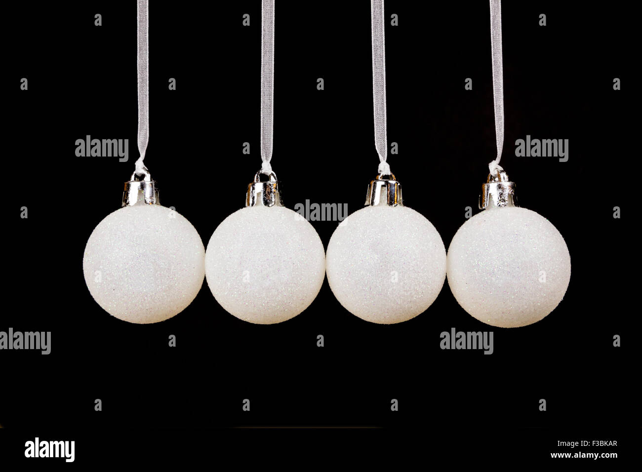 Four white christmas balls hanging in a horizontal row isolated on black background Stock Photo
