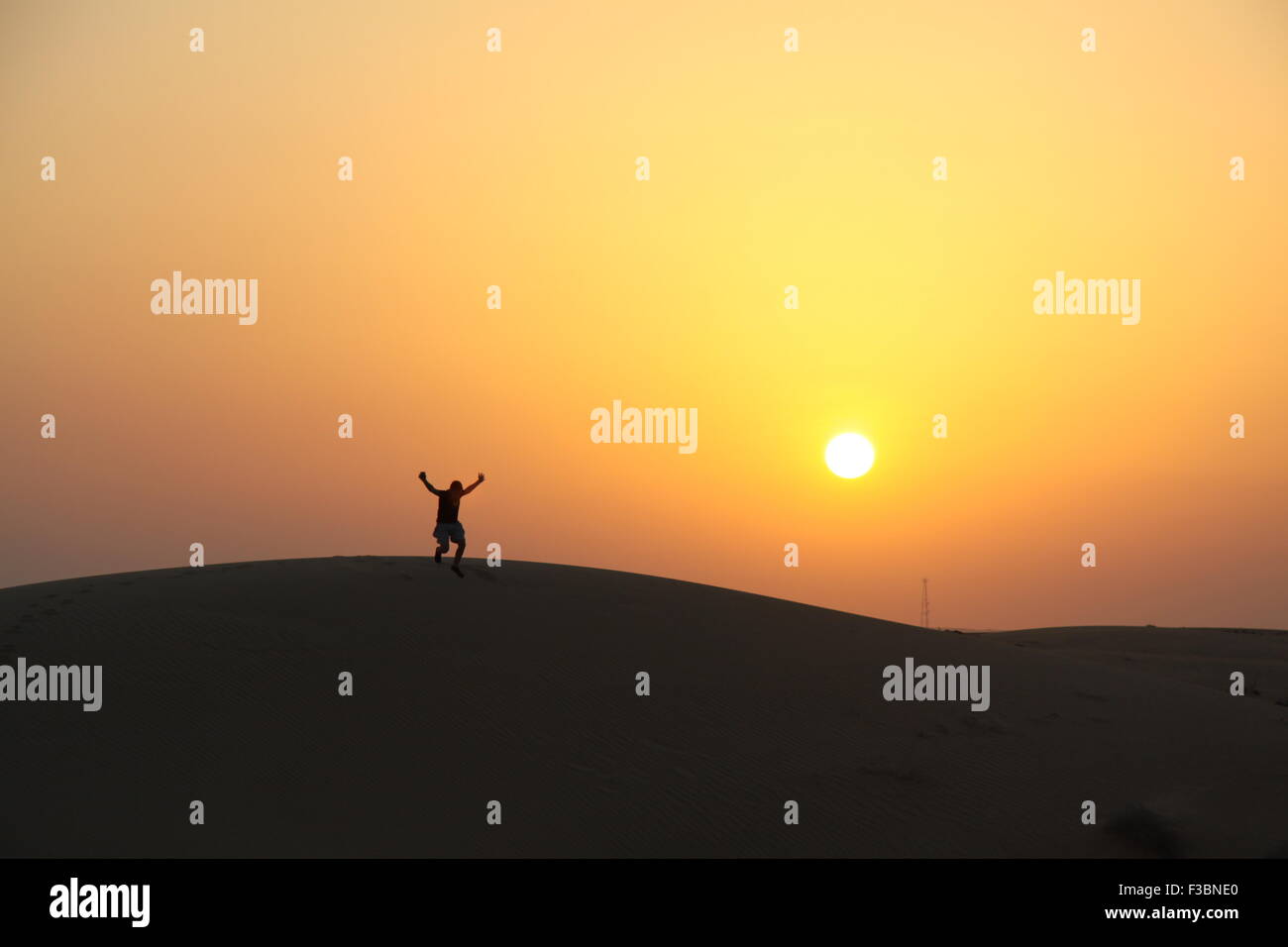 A young man jumping in the Arabian Desert at sunset, near Dubai, UAE. Stock Photo