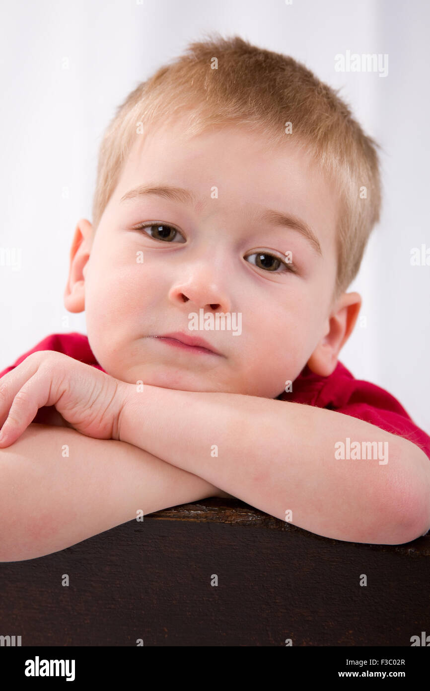 Three year old boy with arms folded over a chair, looking sad and bored