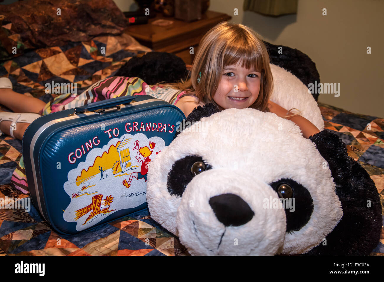 Four year old girl hugging large stuffed panda bear that she's going to sleep with while staying at her grandparent's house Stock Photo