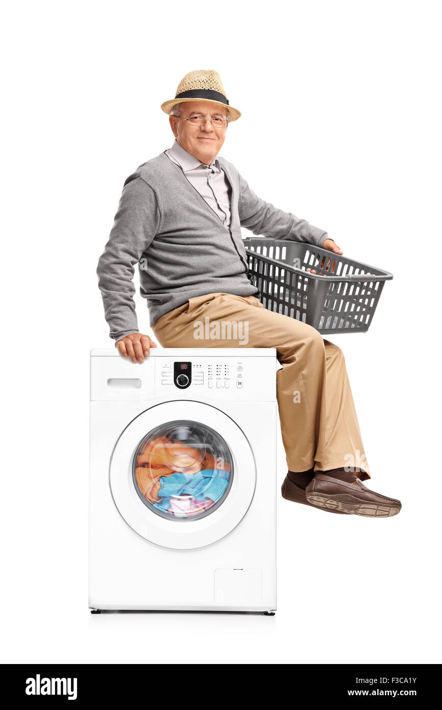 Vertical shot of a senior man waiting for the laundry seated on a washing machine isolated on white background Stock Photo