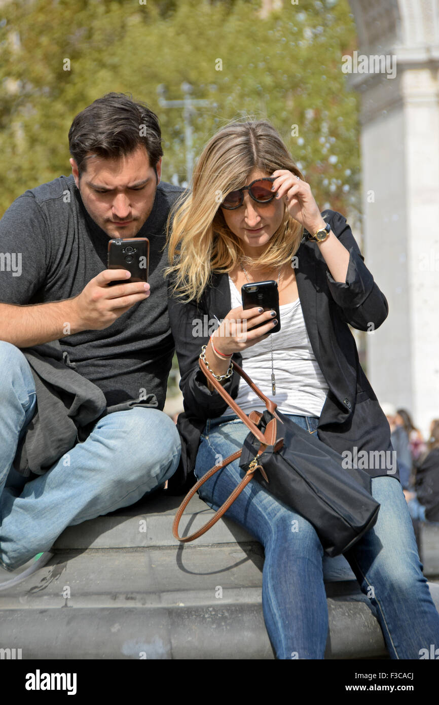 Tourists in Washington Square Park in Greenwich Village ignore each other while check their cell phones. New York City Stock Photo