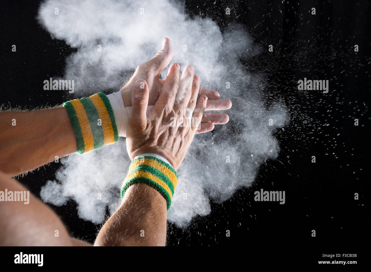 Taped hands of gymnast clapping white chalk powder into a cloud against