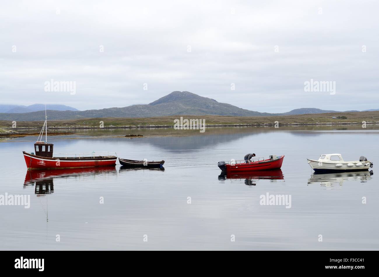 fisherman in a small red boat in early morning light Inishnee Roundstone Connemara County Galway Ireland Stock Photo