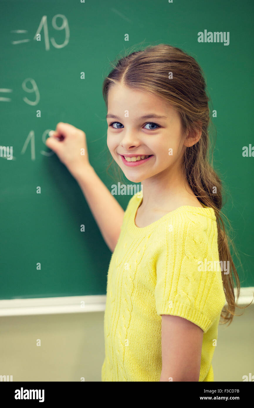 little smiling schoolgirl writing on chalk board Stock Photo