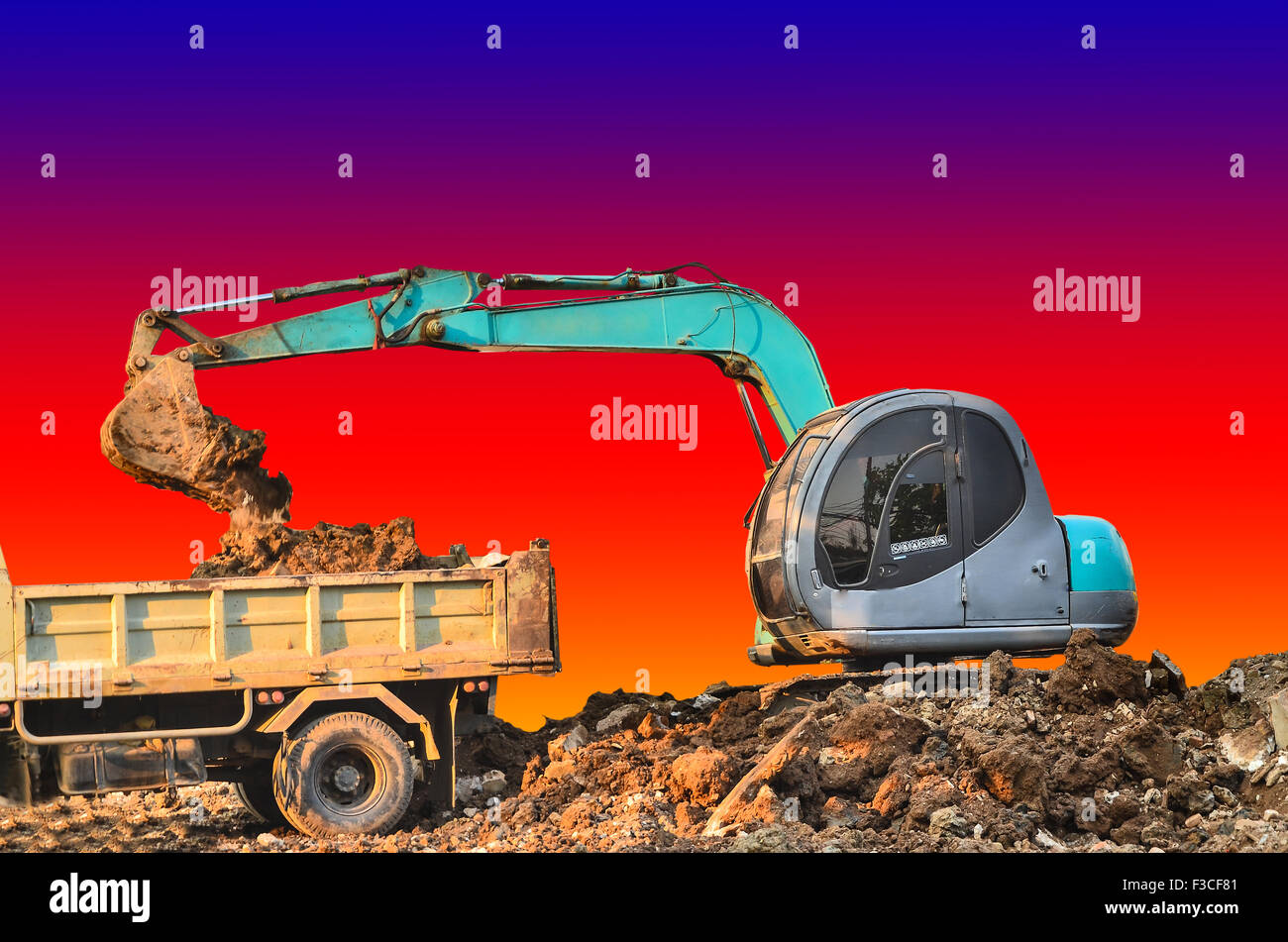 Excavator loading dumper truck tipper in sandpit on sunset Stock Photo