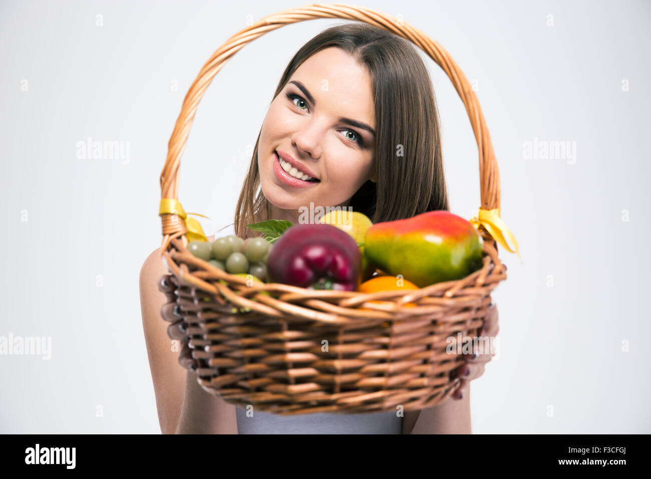Portrait of a smiling charming girl holding basket with fruits isolated ...