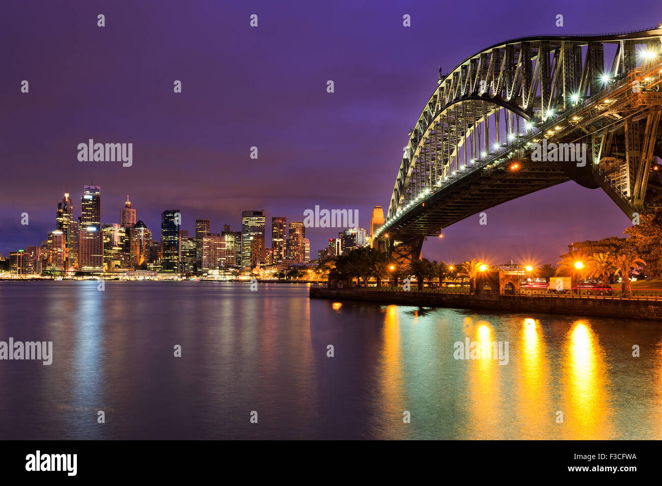 Sydney CBD cityline of illuminated high-rise buildings and harbour bridge with colourful reflection in blurred harbour waters Stock Photo