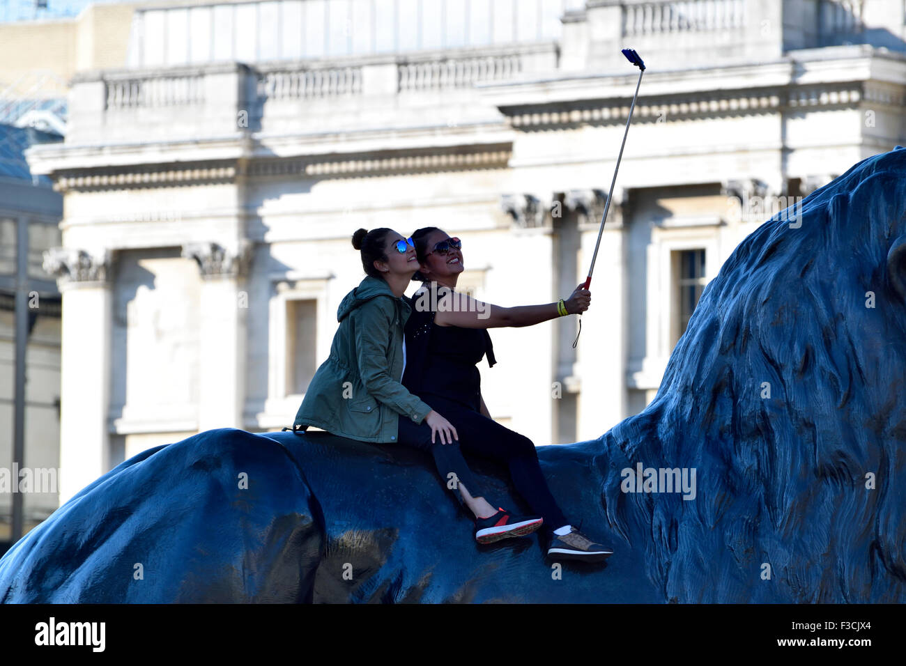 London, England, UK. Two young women sitting on a lion in Trafalgar Square taking a selfie Stock Photo