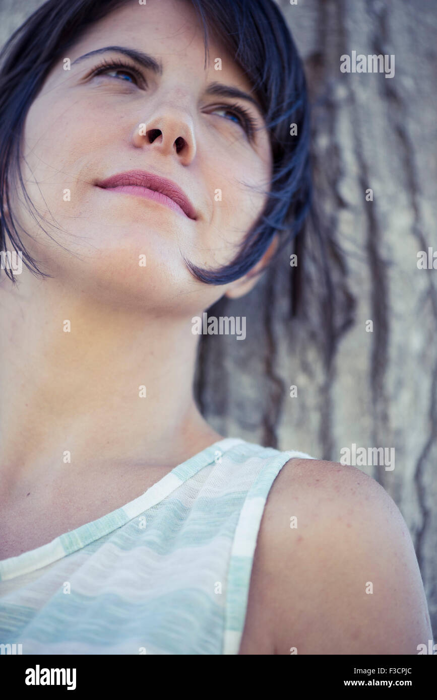 Woman leaning against tree looking away contemplatively Stock Photo