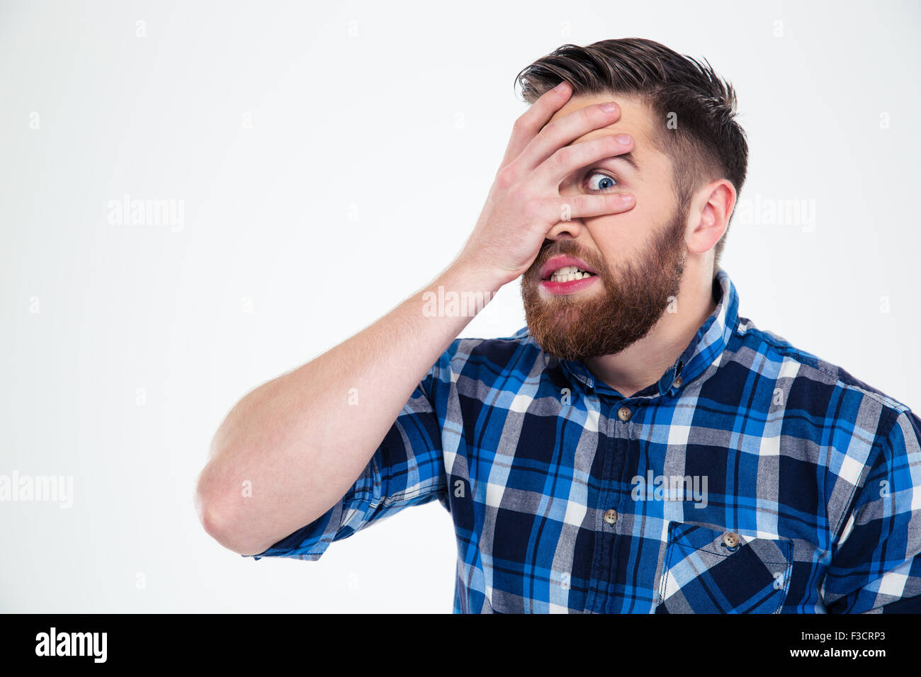 Portrait of a scared man covering his face with palm and looking at camera through fingers isolated on a white background Stock Photo
