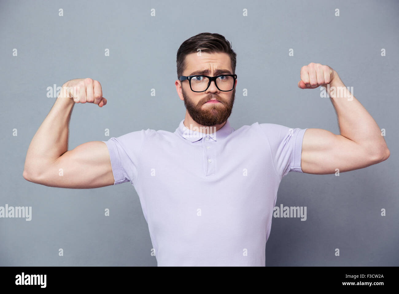 Portrait of a casual man in glasses showing his biceps over gray background Stock Photo