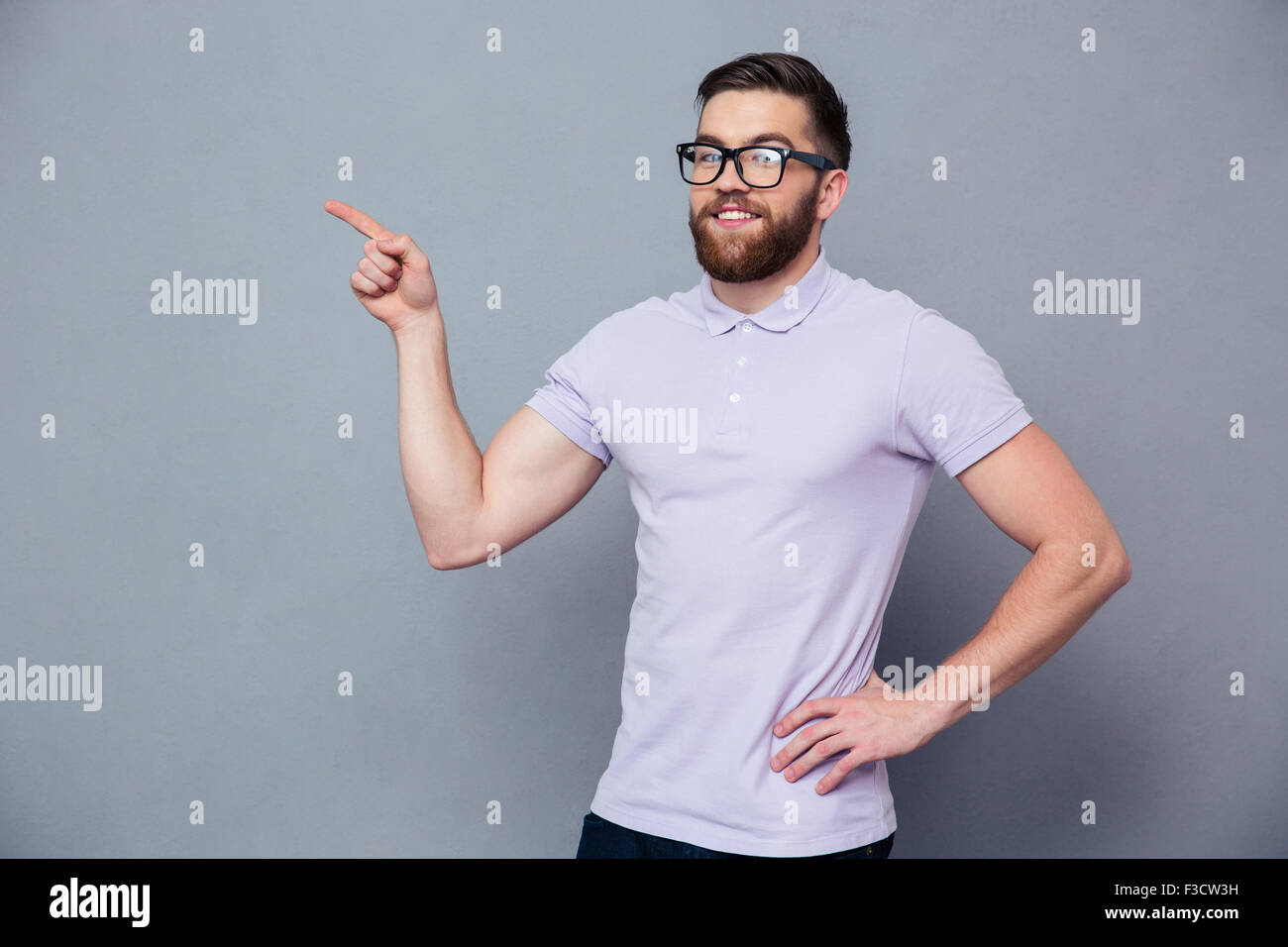 Portrait of a happy casual man in glasses pointing finger away over ...