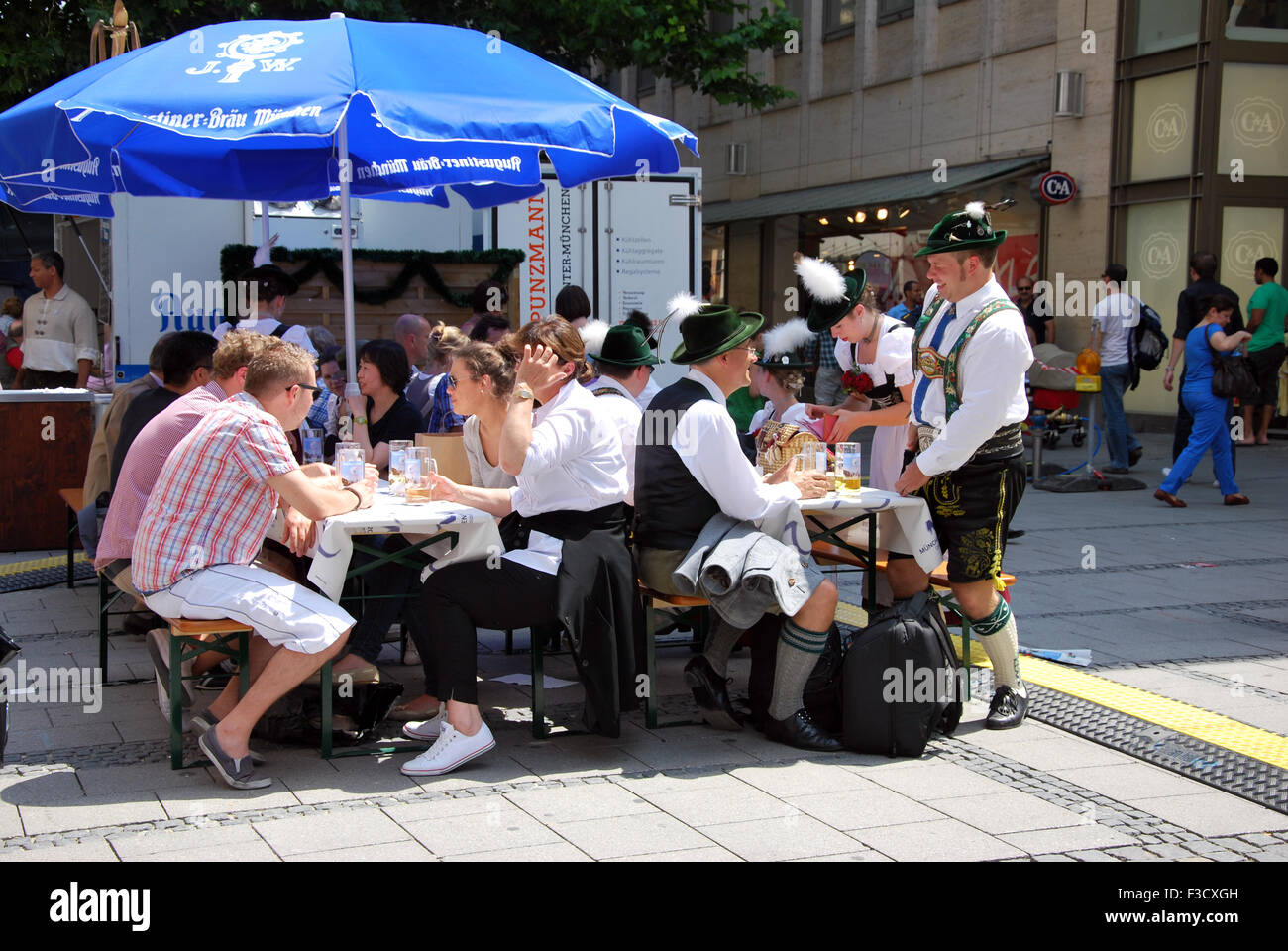 Munich, Germany -July 07: People having bear sitting in the street. Some dressed in traditional Bavarian dress clothes some with Stock Photo