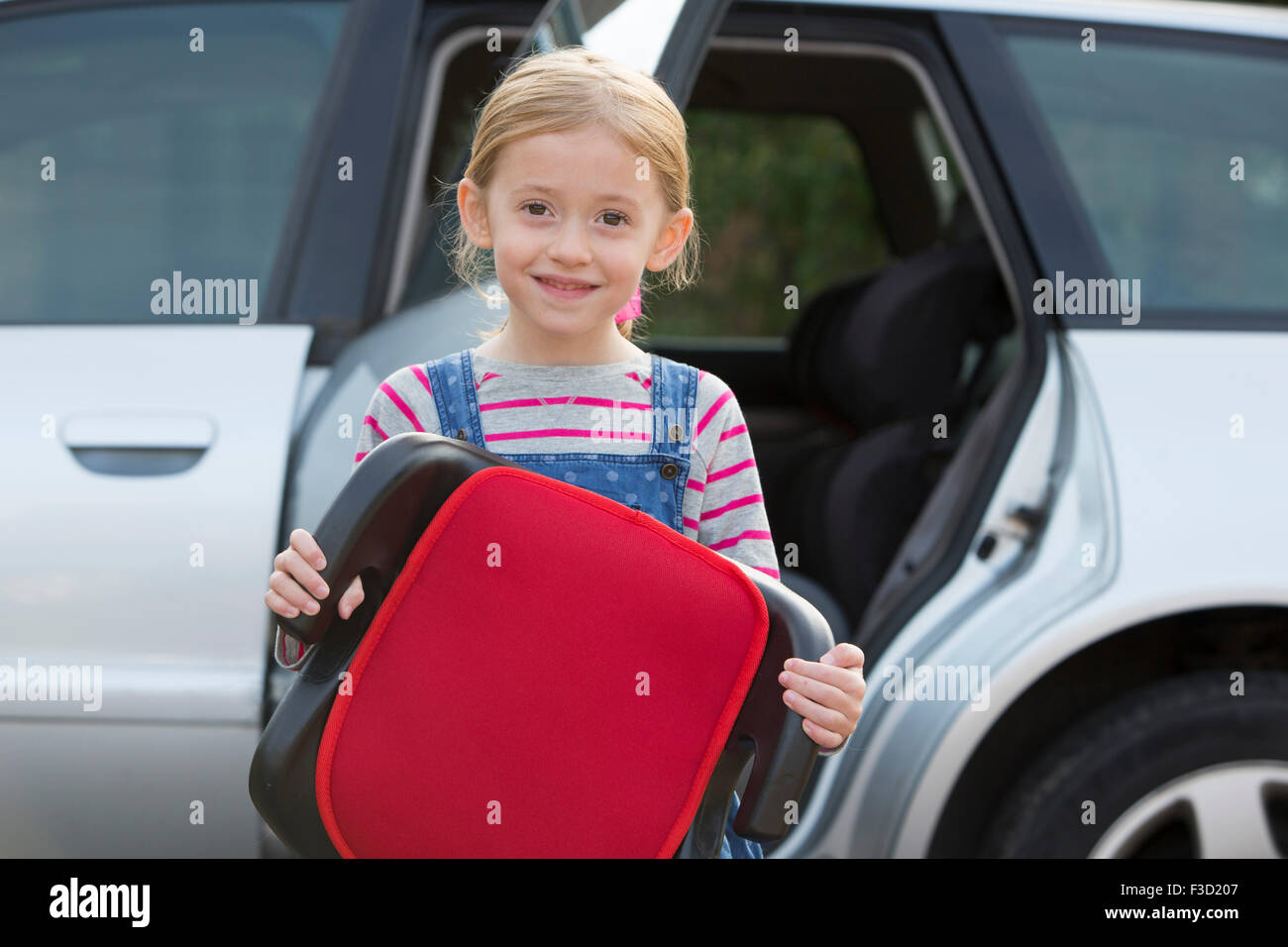 Portrait Of Girl Holding Booster Seat Standing Next To Car Stock Photo