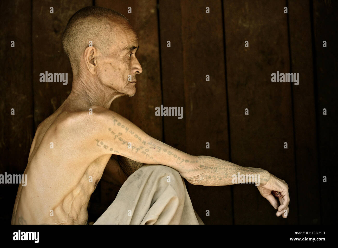 Skinny tattooed man of the Loi tribe sitting inside his wooden house in the village of Wun Nyat, Shan State, Myanmar Stock Photo
