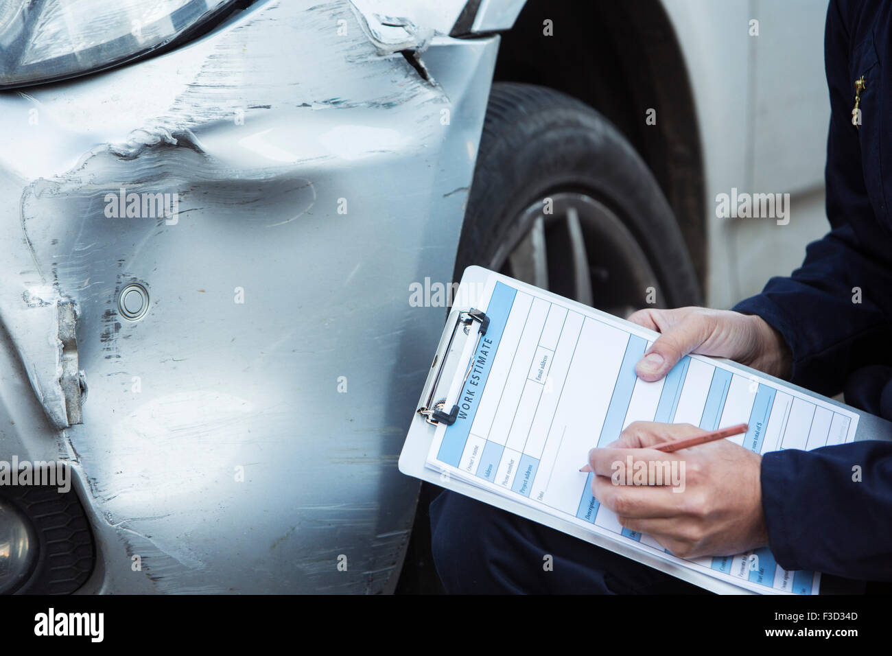 Auto Workshop Mechanic Inspecting Damage To Car And Filling In Repair Estimate Stock Photo