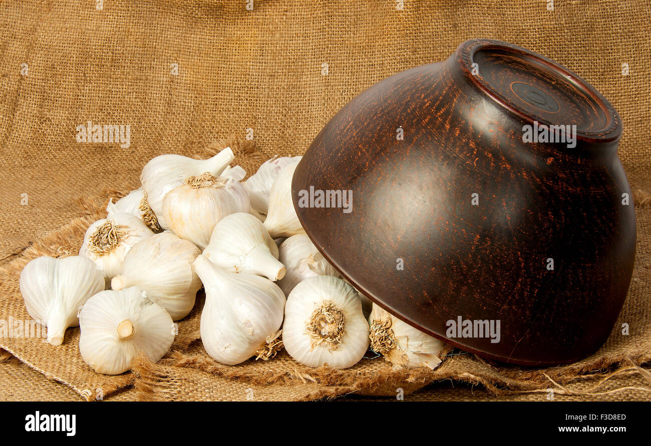 Garlic spill out of a ceramic bowl on sackcloth Stock Photo