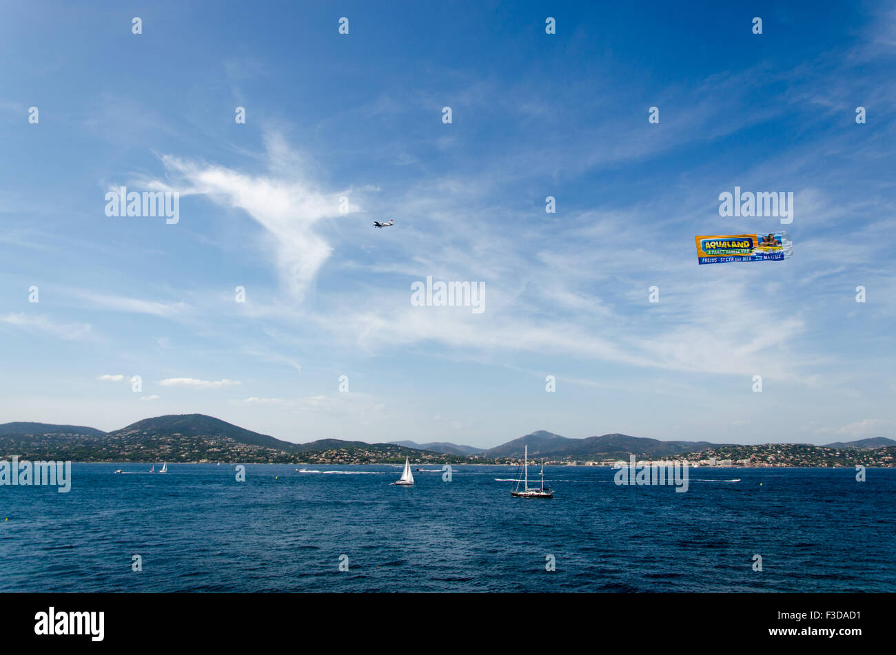 Beautiful blue sea, blue sky, mountain, sailing boats, and an advertising plane on the sky at Saint-Tropez Stock Photo