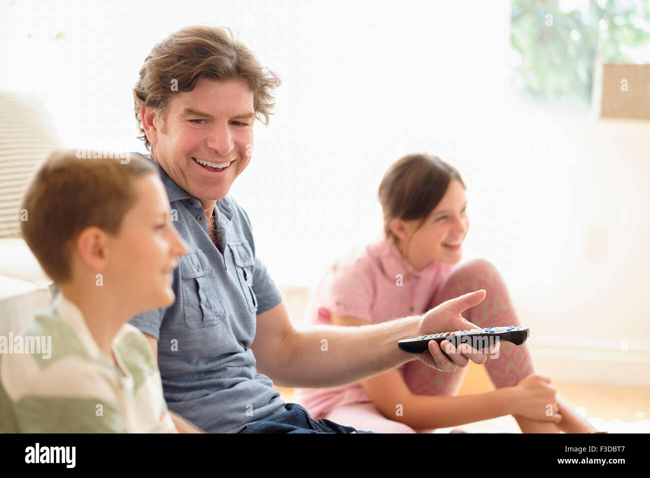 Children (8-9, 10-11) watching TV with their father Stock Photo