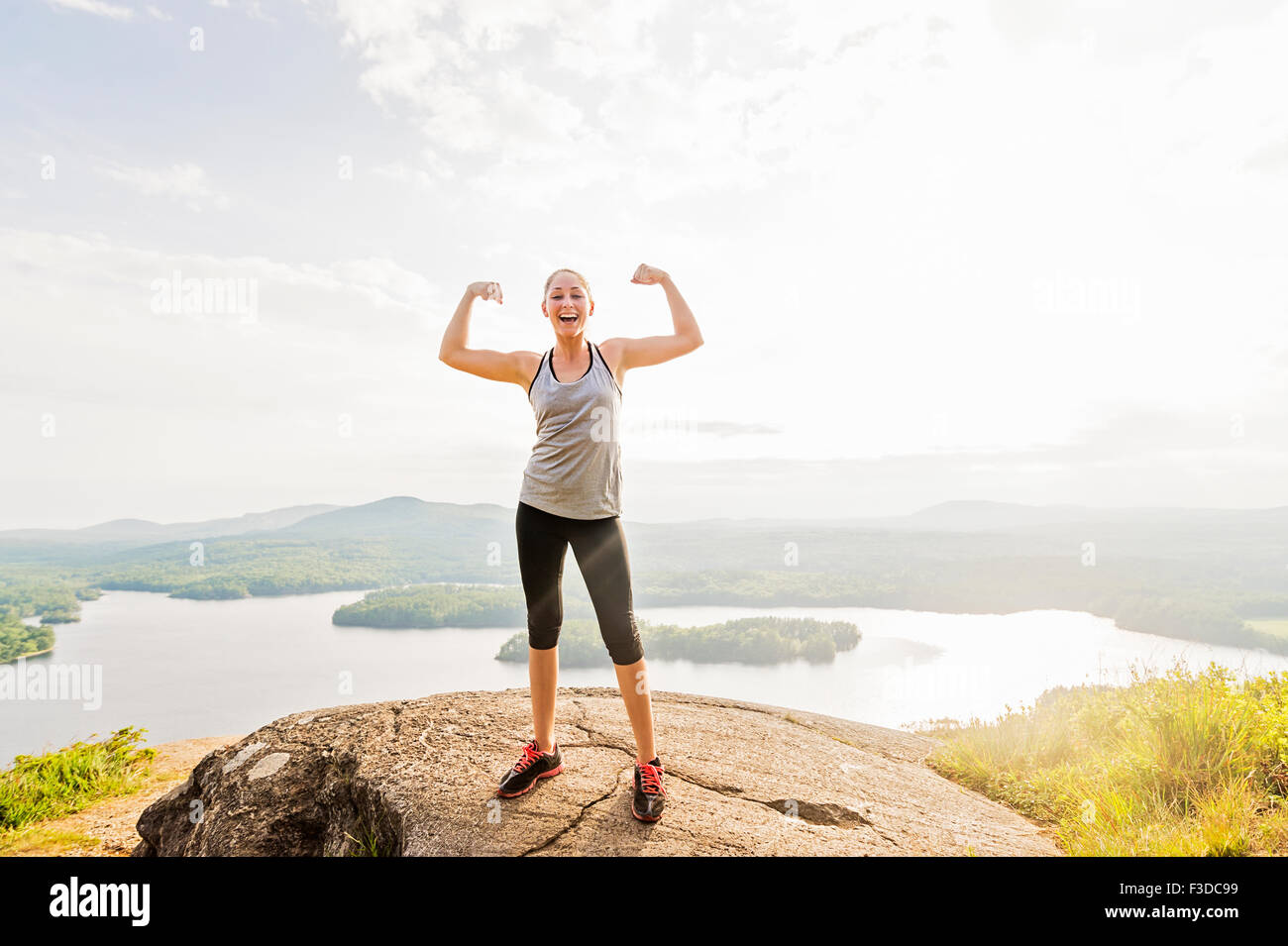 Young woman standing on top of mountain and flexing muscles Stock Photo