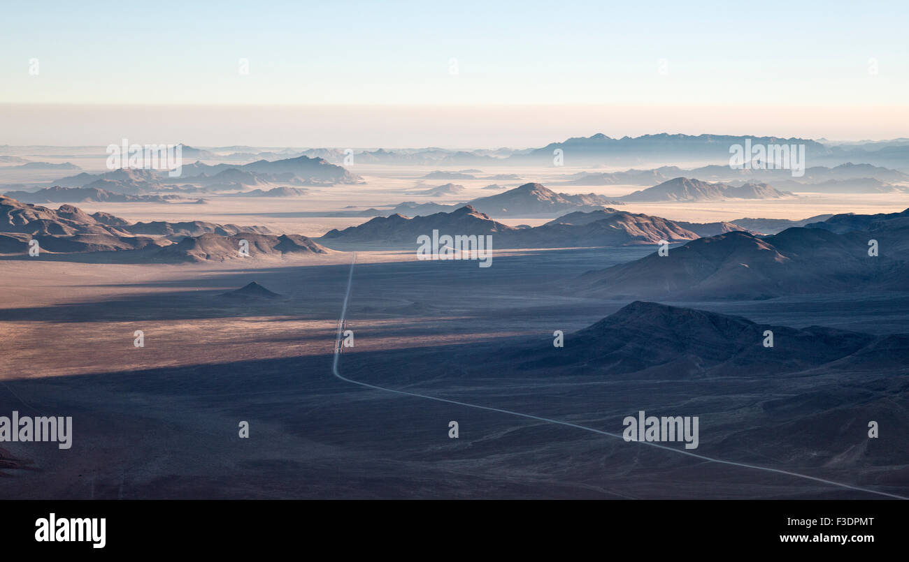Isolated mountain ridges and C27 gravel road, edge of Namib Desert, coastal fog behind, aerial view, NamibRand Nature Reserve Stock Photo