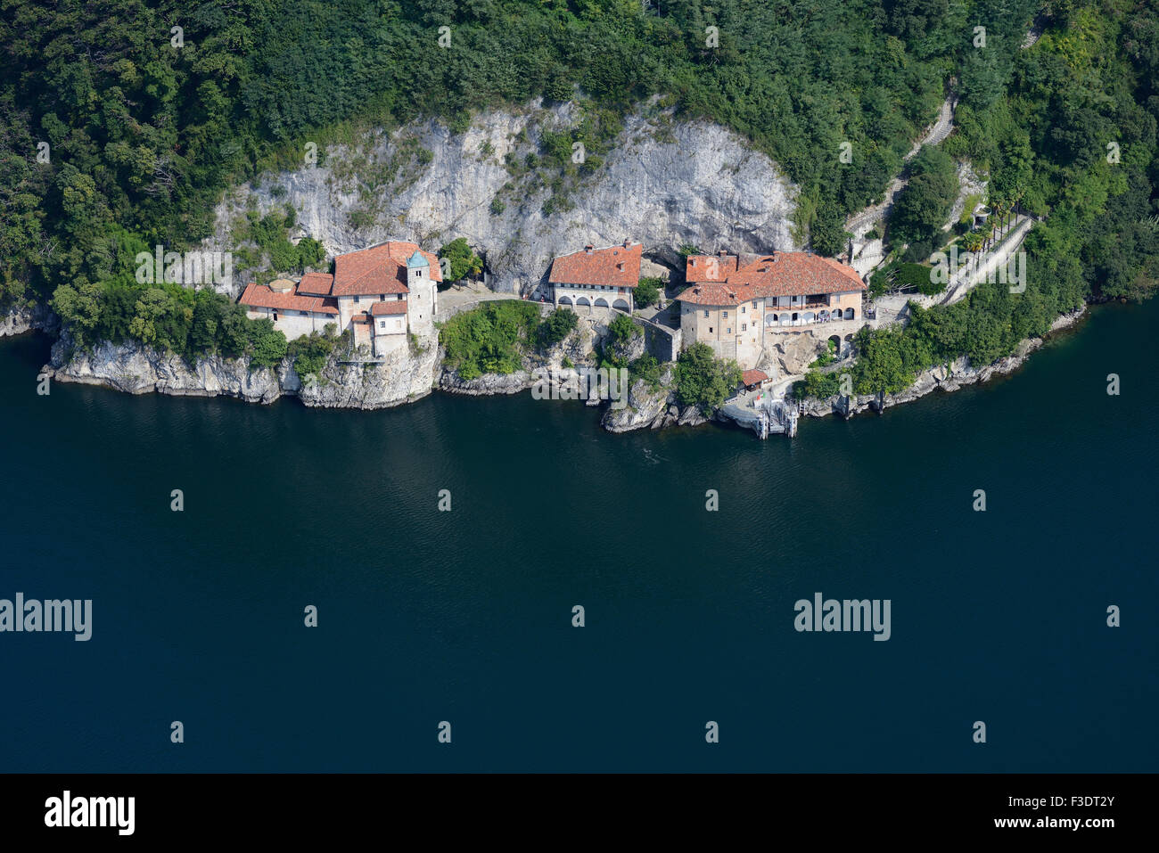 AERIAL VIEW. Monastery on a cliff face above the shore of Lake Maggiore. St Catherine Hermitage, Leggiuno, Province of Varèse, Lombardy, Italy. Stock Photo