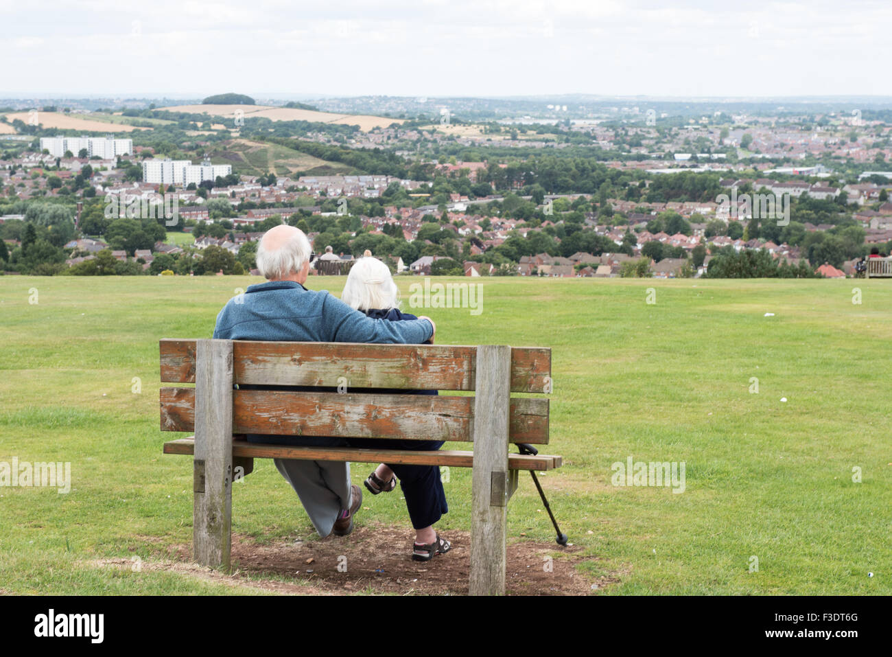Loving elderly couple looking at the city from hillside bench Stock Photo