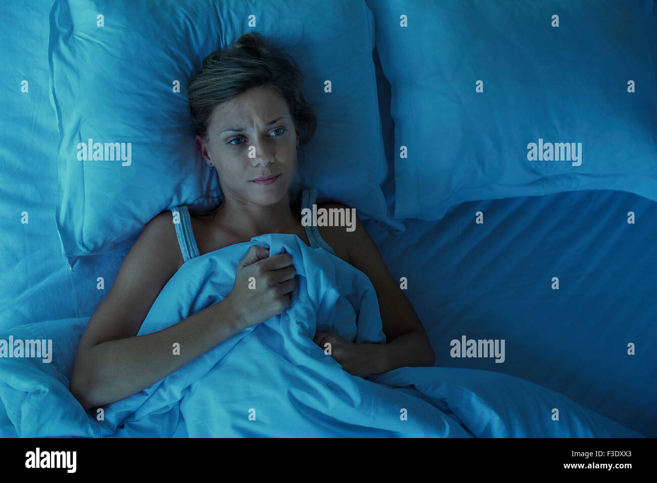 Woman lying alone in bed with upset expression on face Stock Photo