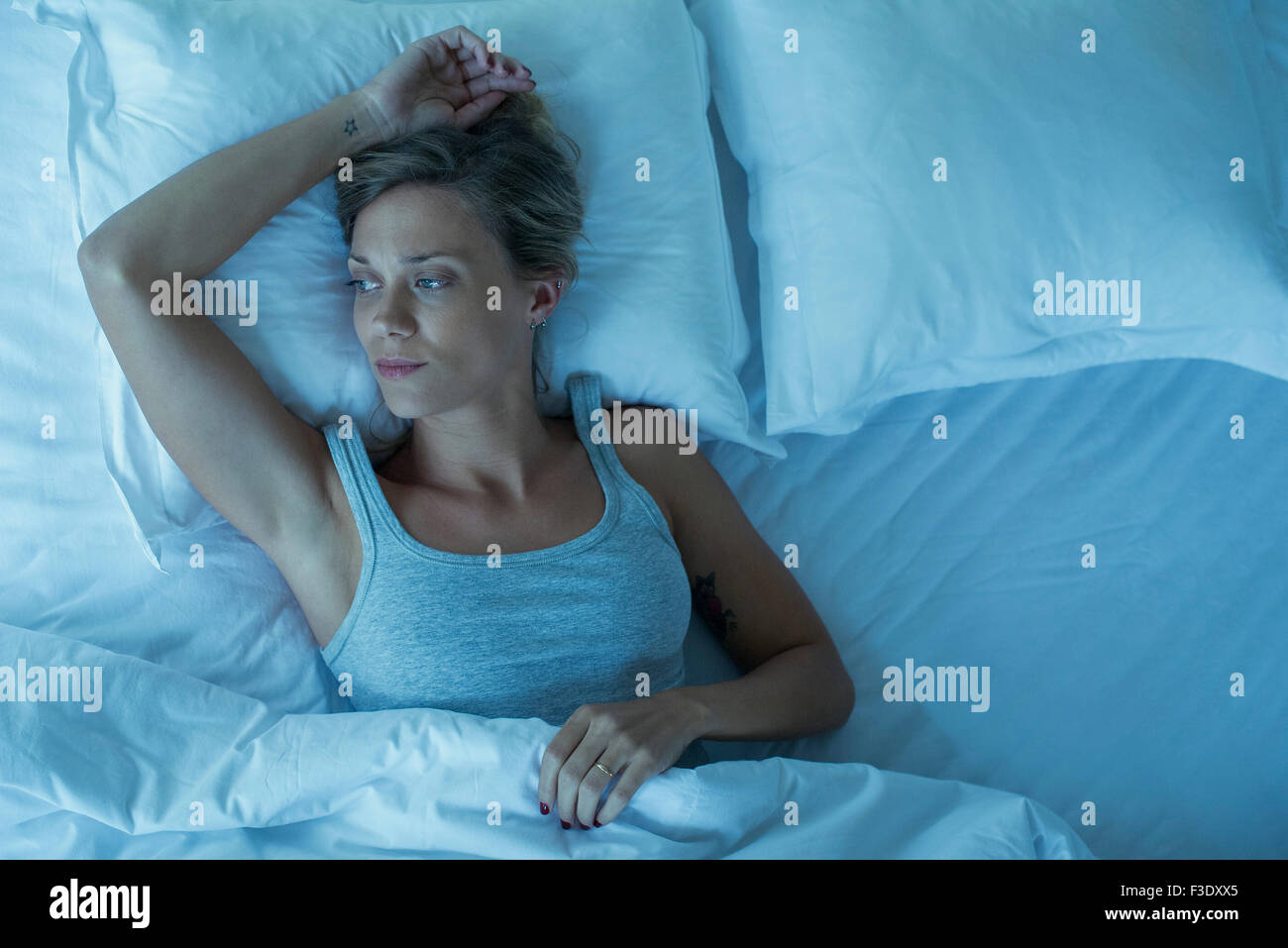 Woman lying alone in bed, looking away in thought Stock Photo