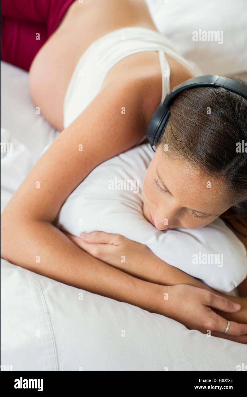 Pregnant woman lying on bed, listening to headphones Stock Photo