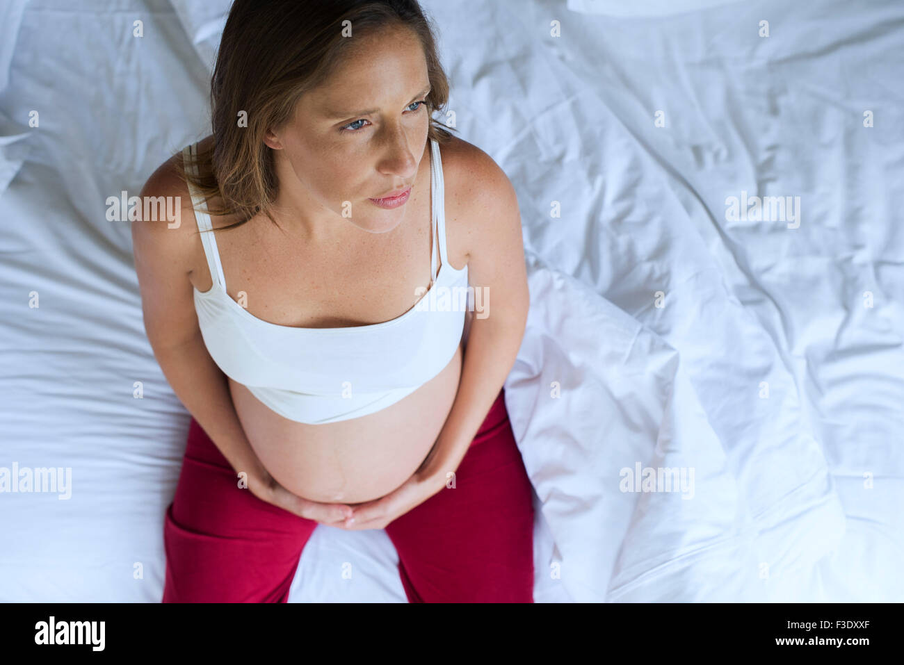 Pregnant woman sitting on bed with hands on stomach Stock Photo