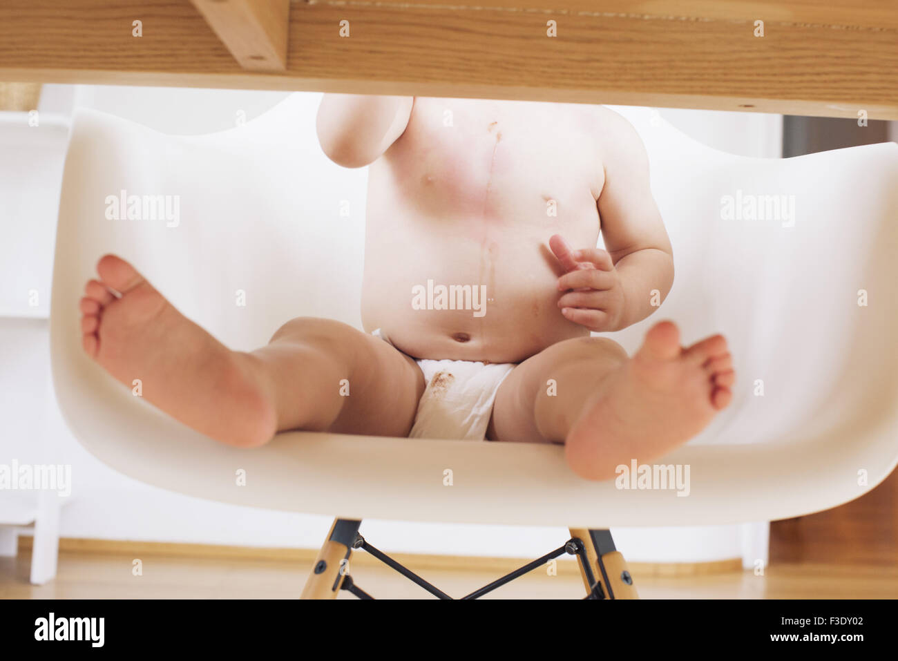 Baby sitting at table in diaper, cropped Stock Photo