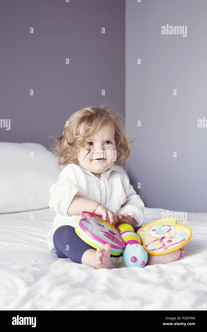 Baby girl sitting on bed playing with toy butterfly Stock Photo