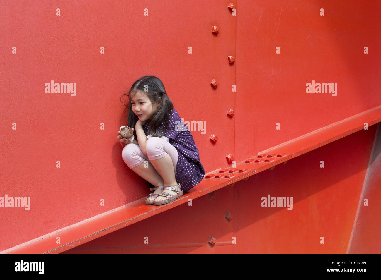 Little girl perched on ledge surreptitiously eating cupcake Stock Photo
