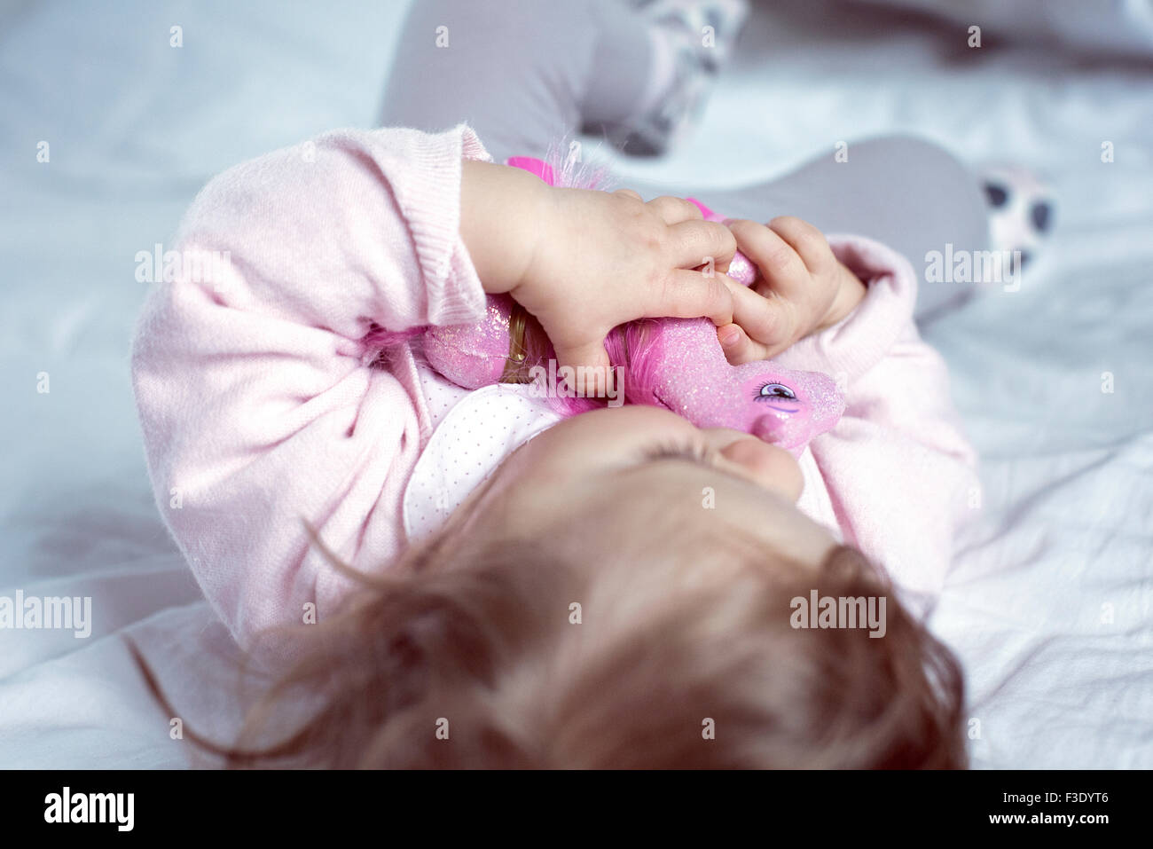 Baby girl lying on bed with toy in arms Stock Photo
