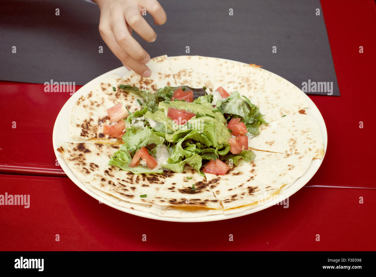Child's hand reaching for quesadilla on plate Stock Photo