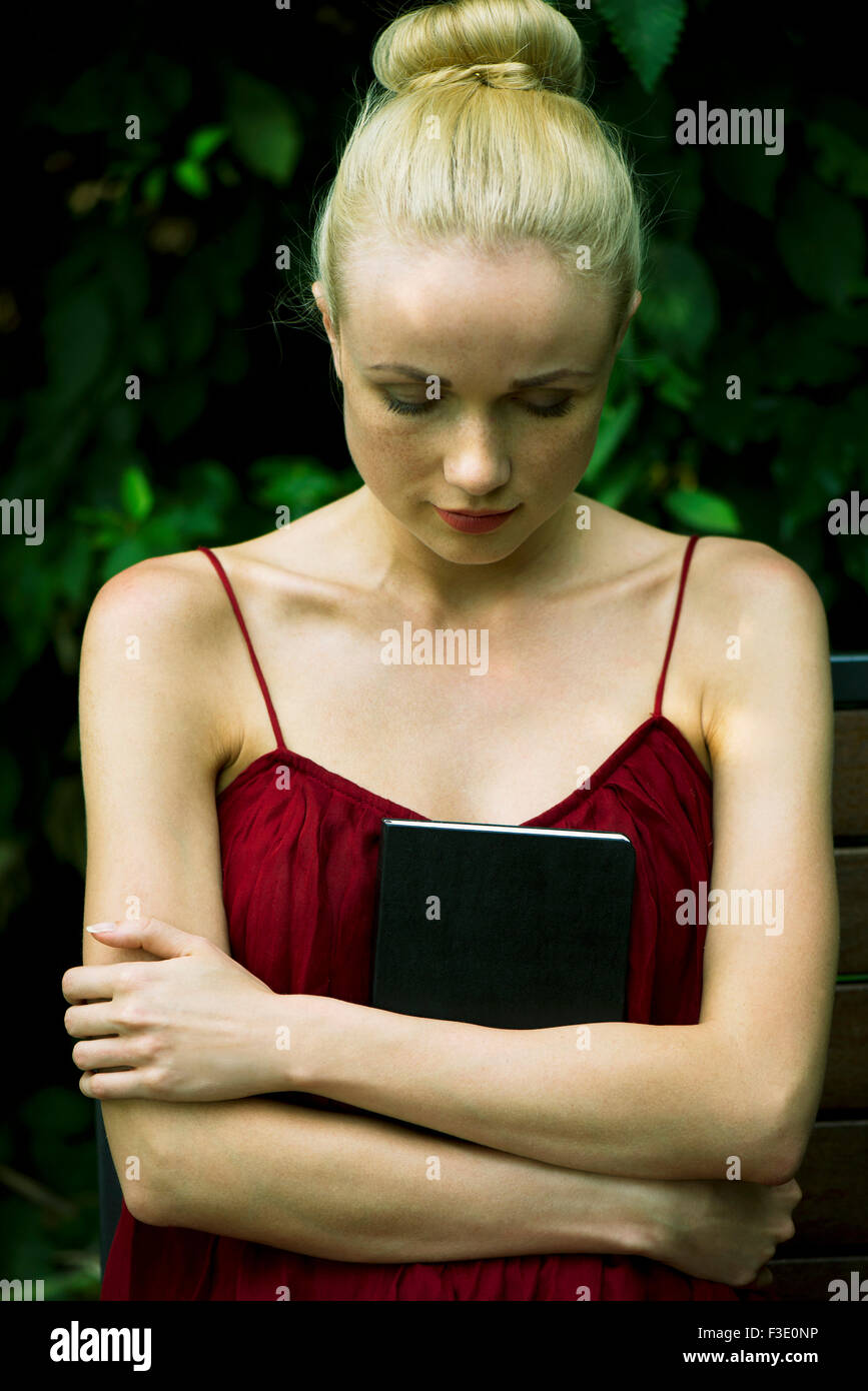 Young woman holding diary against chest, looking down Stock Photo