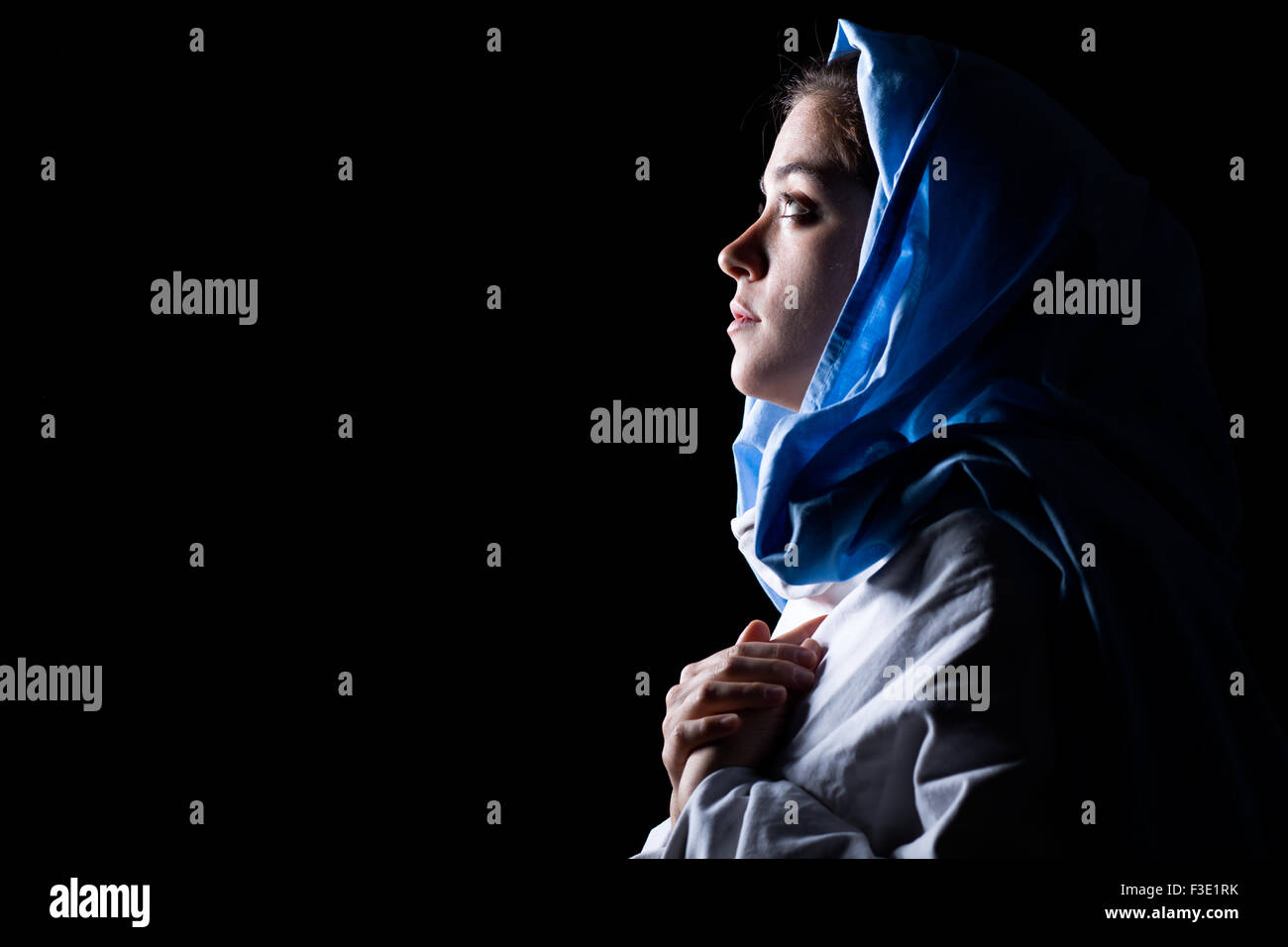 Virgin Mary with Blue Veil Praying on Black Background Stock Photo