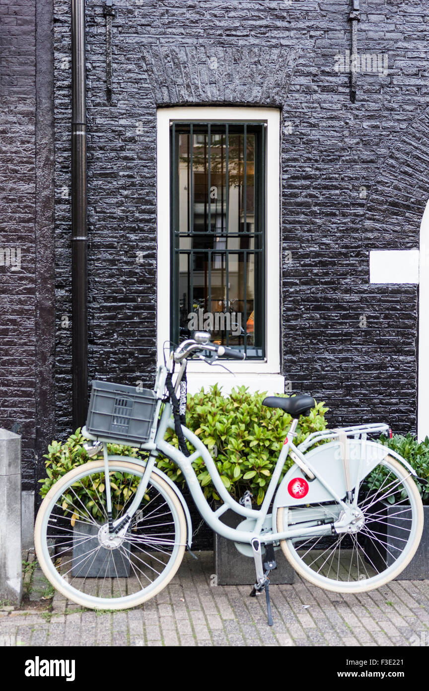 A white bicycle is parked outside of a black house in Amsterdam, The Netherlands. Stock Photo