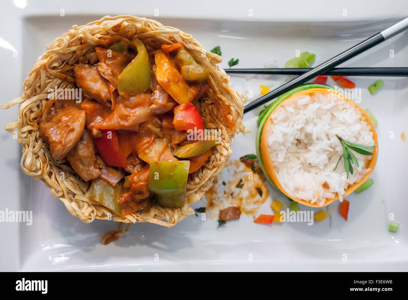 Chinese dish; chicken with sweet green peppers in a fried noodle nest and steamed rise decorated with cucumber and carrot aside Stock Photo
