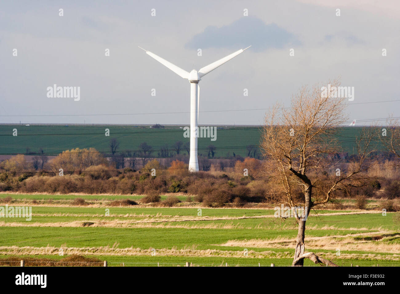 England, Ramsgate. Single wind-turbine seen from the distance, sunlit landscape in foreground, but dark behind, road on the horizon. Stock Photo