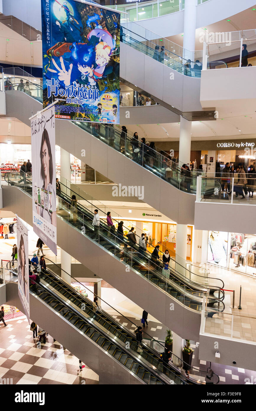 Nishinomiya Gardens, Fashionable shopping centre, Japan. Atrium at one end with escalators, several floors and advertising signs. Busy. Stock Photo