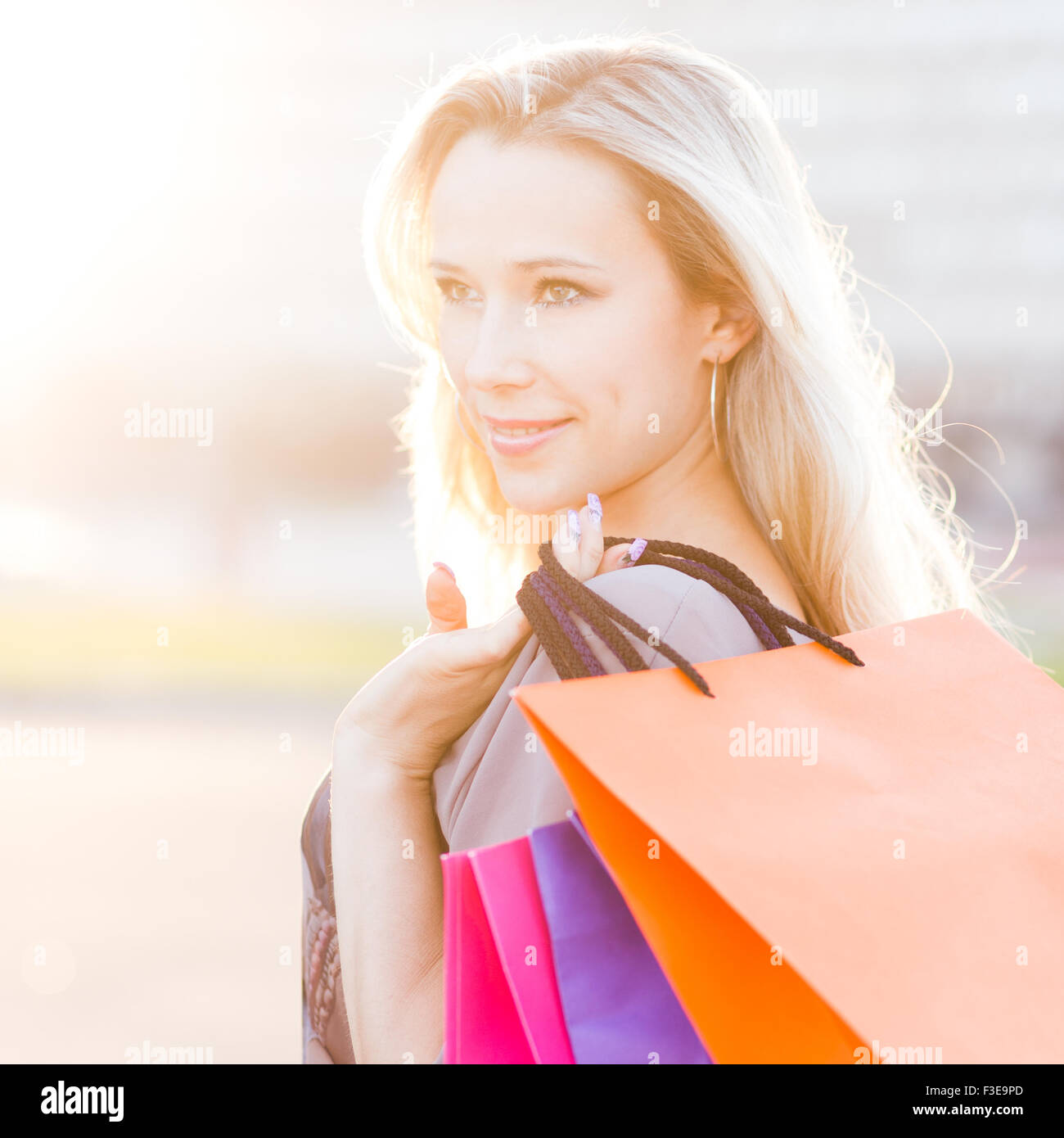 Young woman stands with shopping bags against sun. Beautiful adult girl