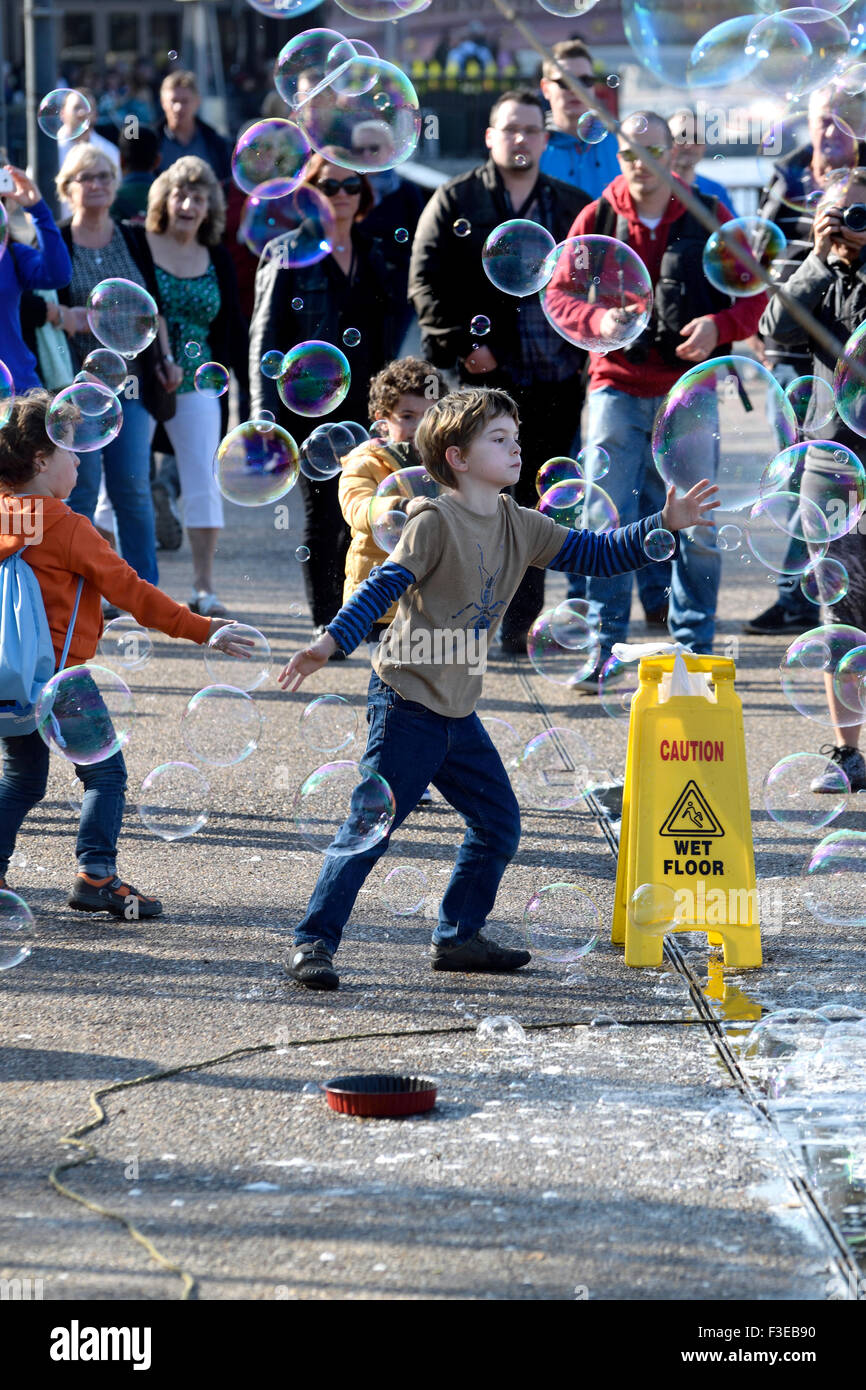 London, England, UK. Young boy chasing bubbles made by a street entertainer, South Bank Stock Photo