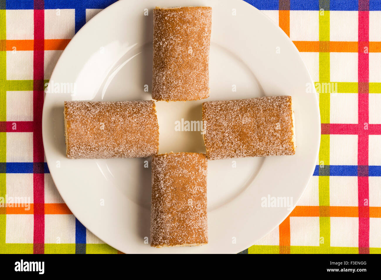 Four cakes filled with cream and rolled forming a cross on a colorful striped tablecloth Stock Photo