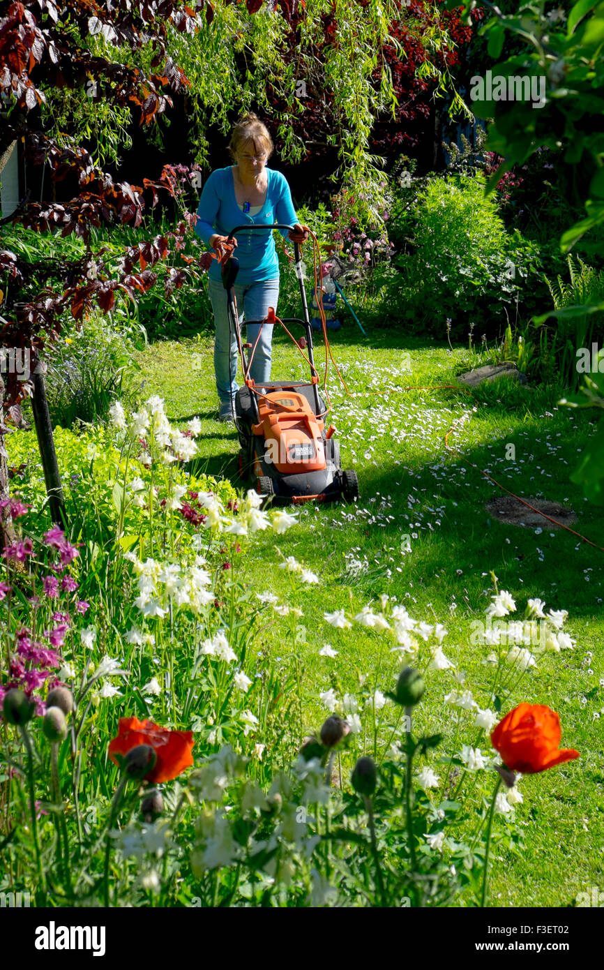 Elderly woman mowing lawn with electric mower, Wales, UK Stock Photo