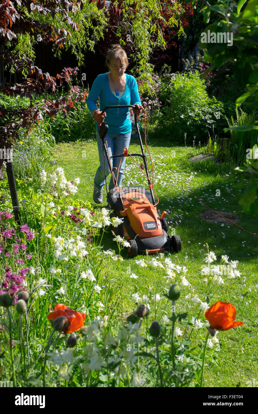 Elderly woman mowing lawn with electric mower, Wales, UK Stock Photo