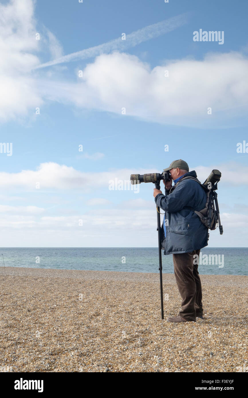 A man birdwatching on a pebble beach at Salthouse, Norfolk, with a large camera and a monopod. Stock Photo