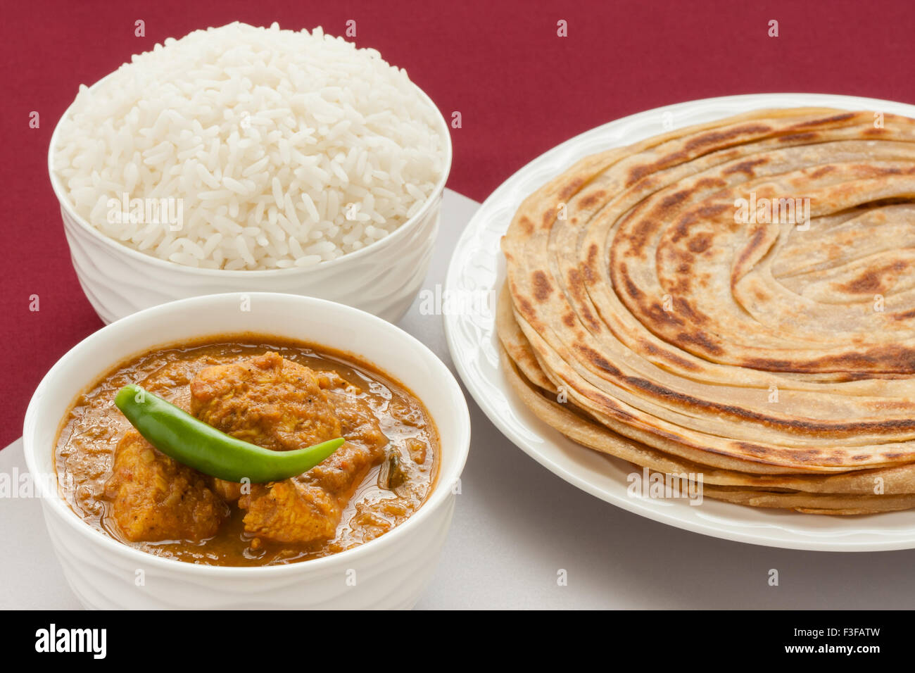 Closeup view of Indian chicken curry meal with rice and wheat parotta (Indian bread). Green chilli used as garnish. Stock Photo